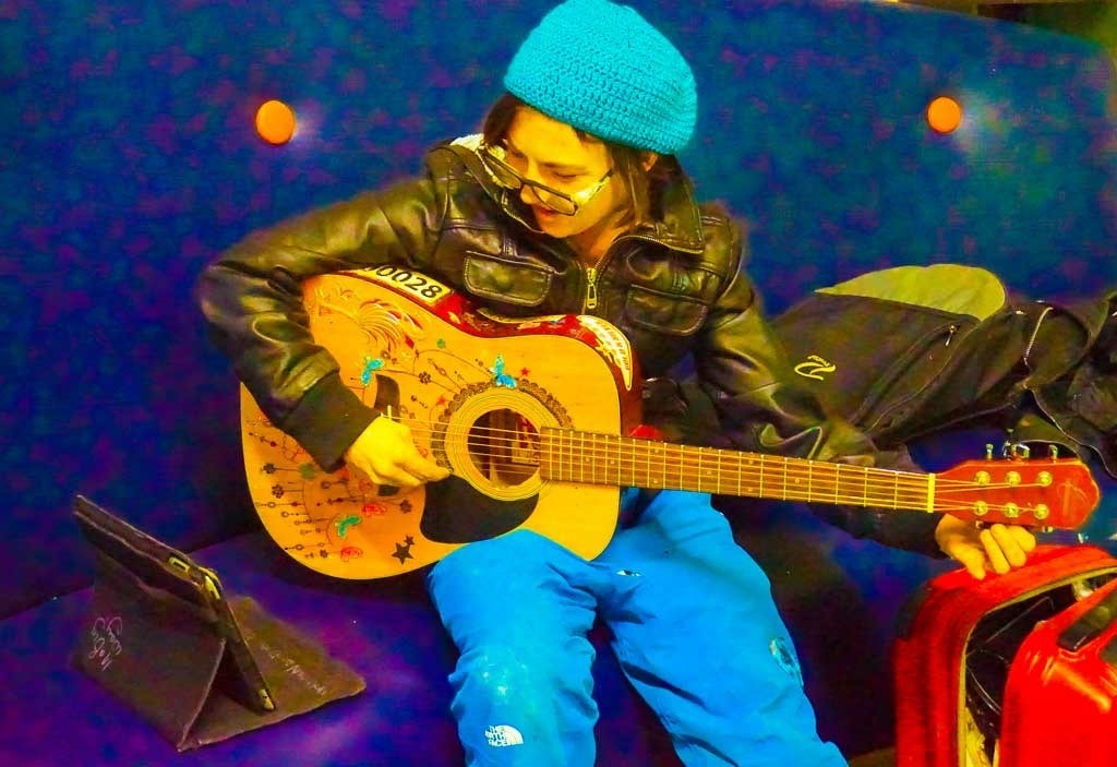 Musician in a teal toque playing an acoustic guitar