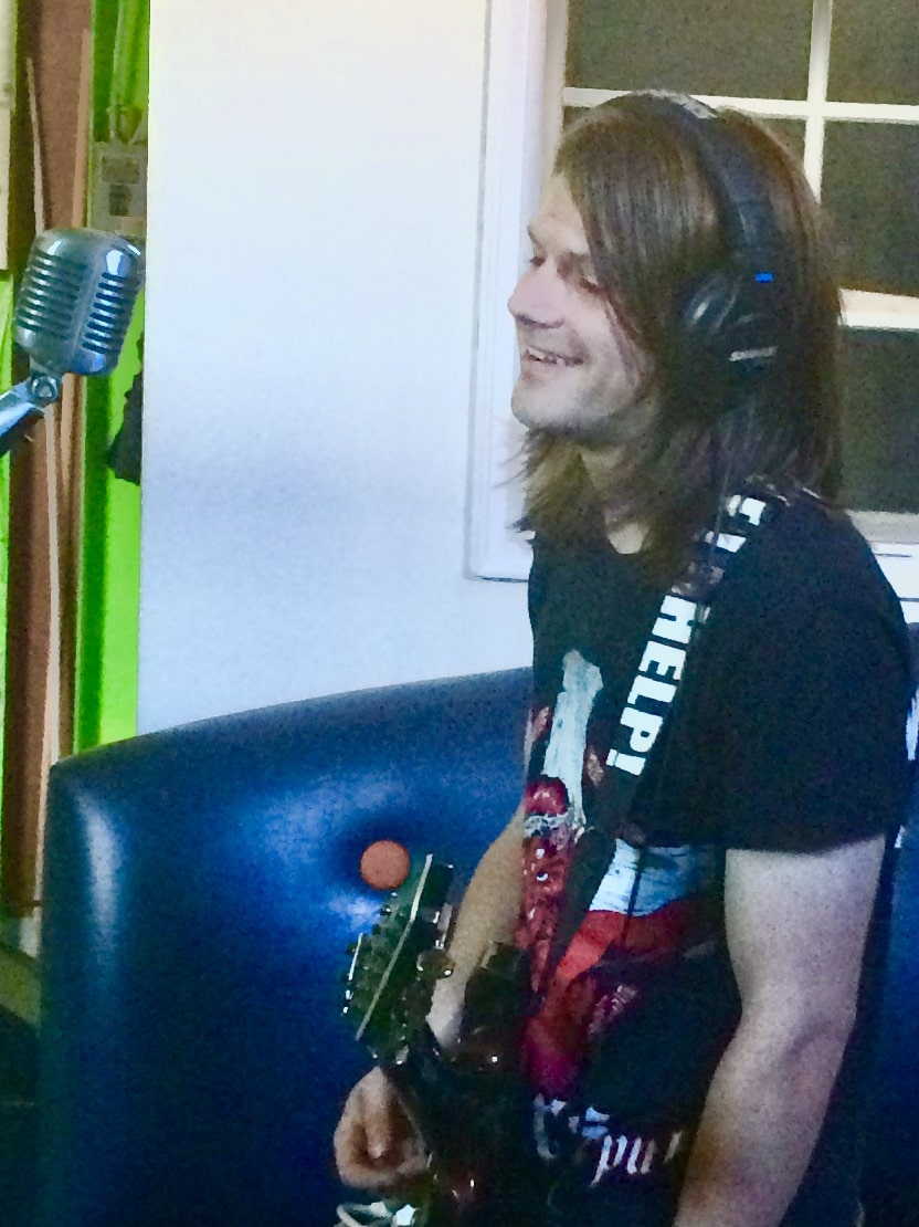 Long-haired guitarist in headphones, smiling mid-take