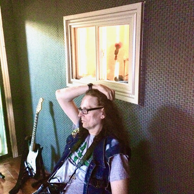 Musician leaning back against the studio wall beside a guitar