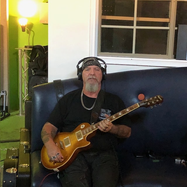 Bearded guitarist in headphones with a gold-top Les Paul on the couch