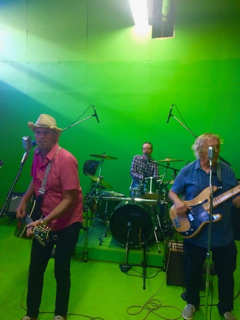 Three-piece band in cowboy hat and ball caps playing under the studio lights