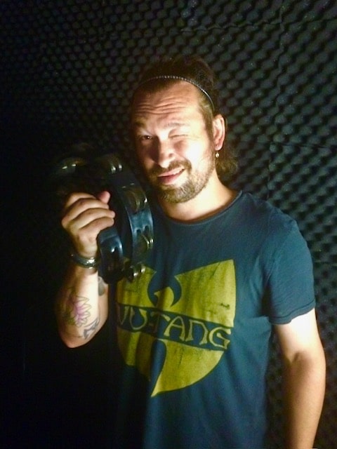 Bearded musician in a Wu-Tang shirt against acoustic foam